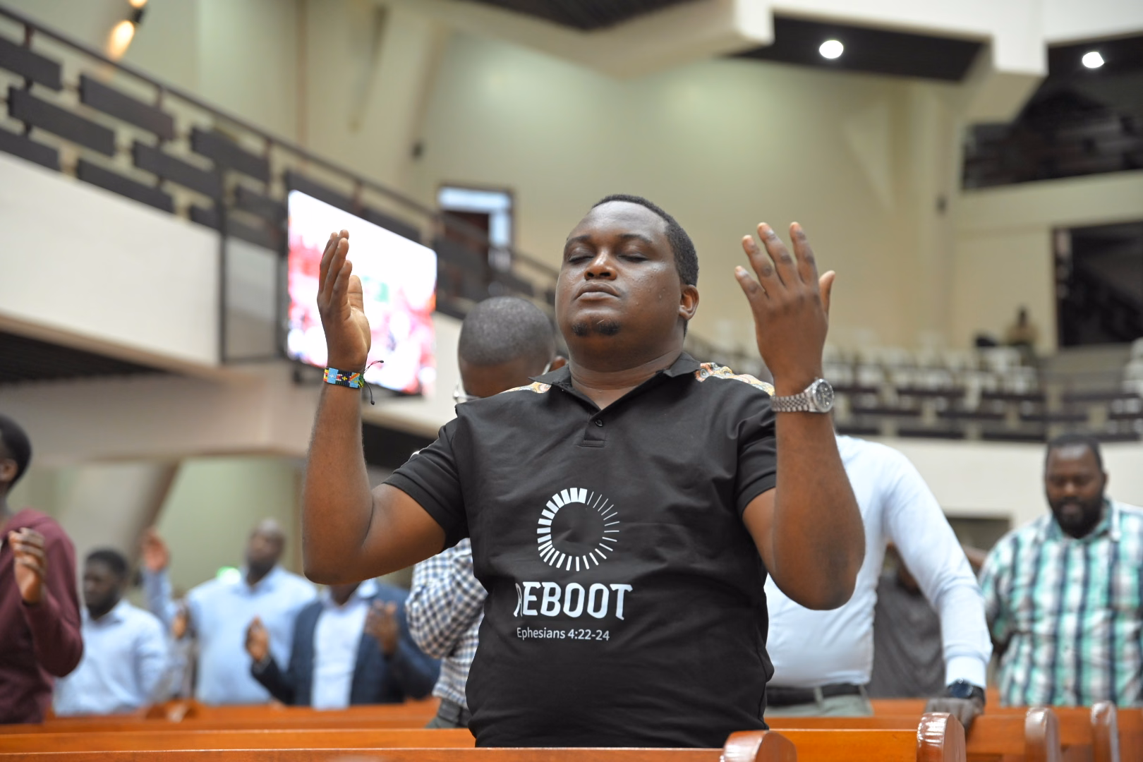 A young man praying with his hands raised among other men at the conference